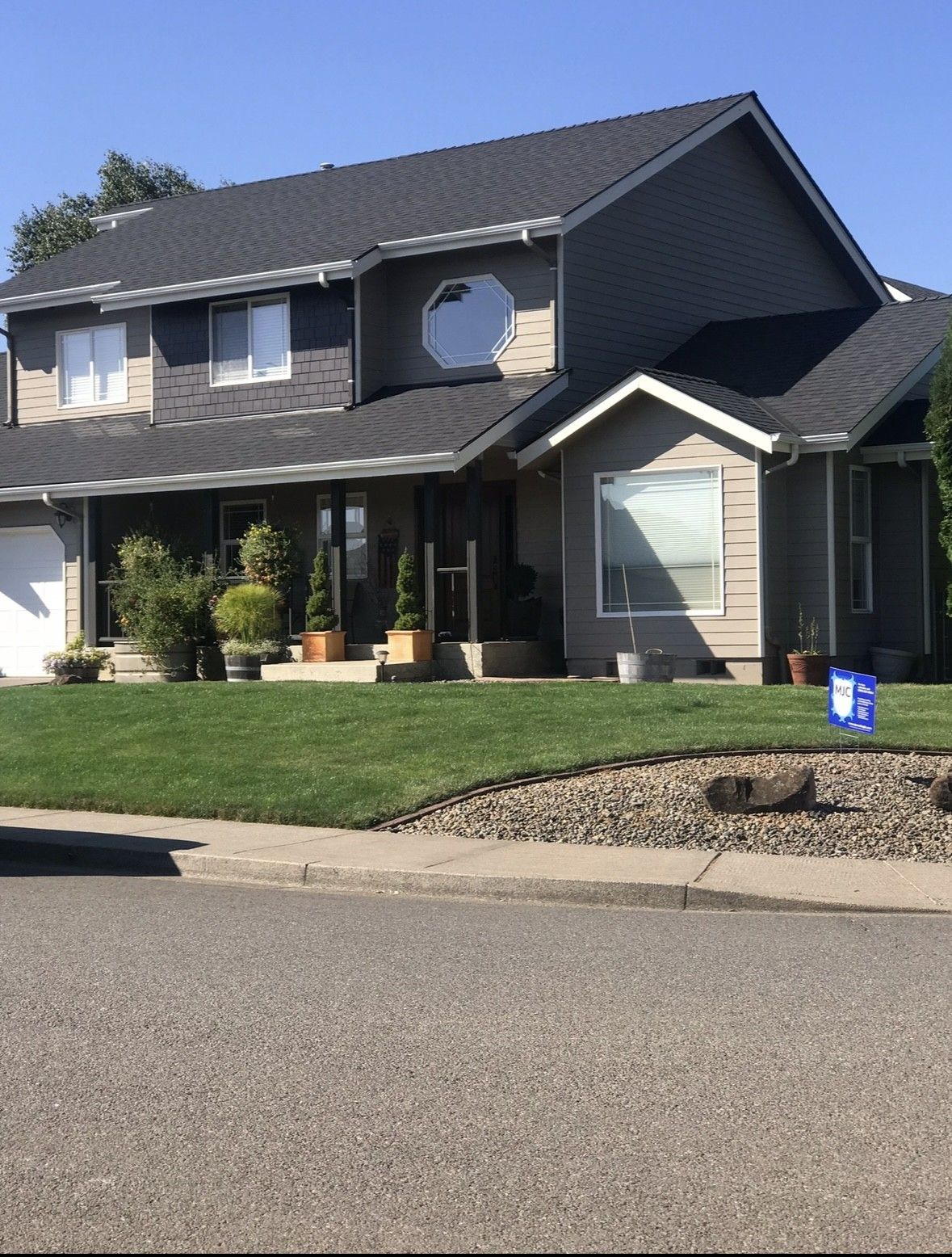 Two-story gray house with a front porch, manicured lawn, and blue sky.