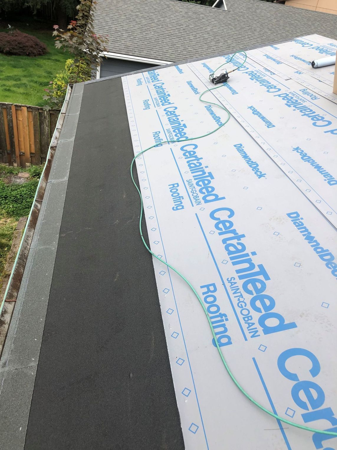 Roof under construction with black underlayment and white roofing membrane along the edge