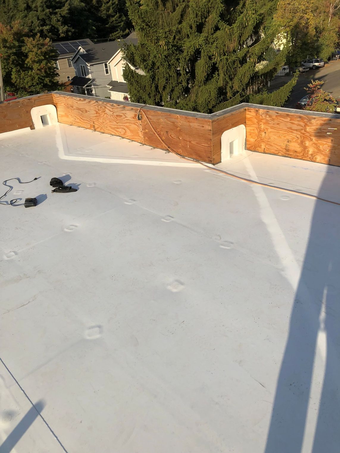 Flat rooftop with white coating, brick parapet walls, and tree shadows in the background.