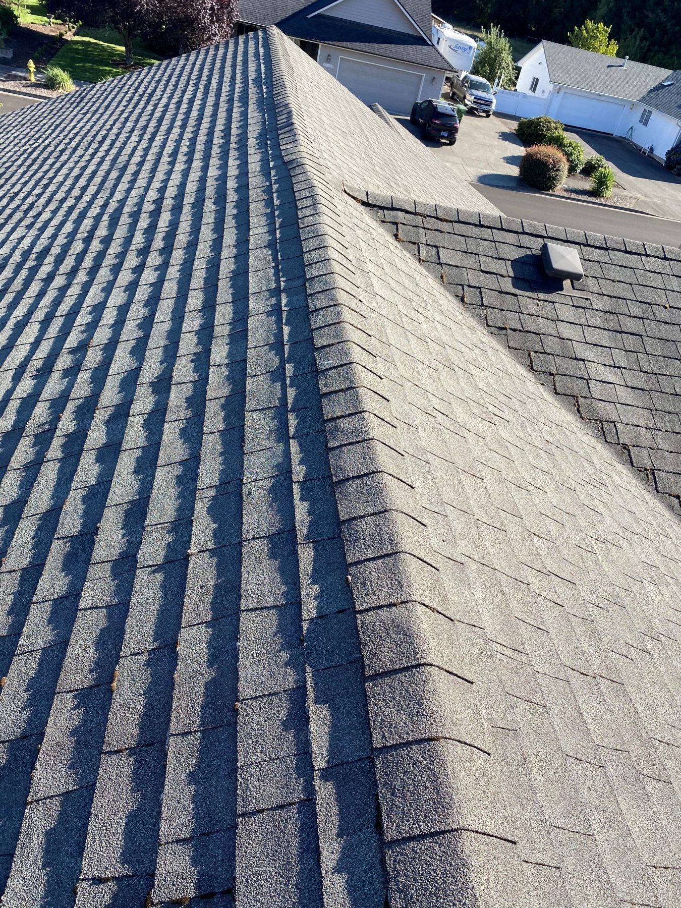 Rooftop with gray shingles and a central ridge, viewed from above in a suburban neighborhood