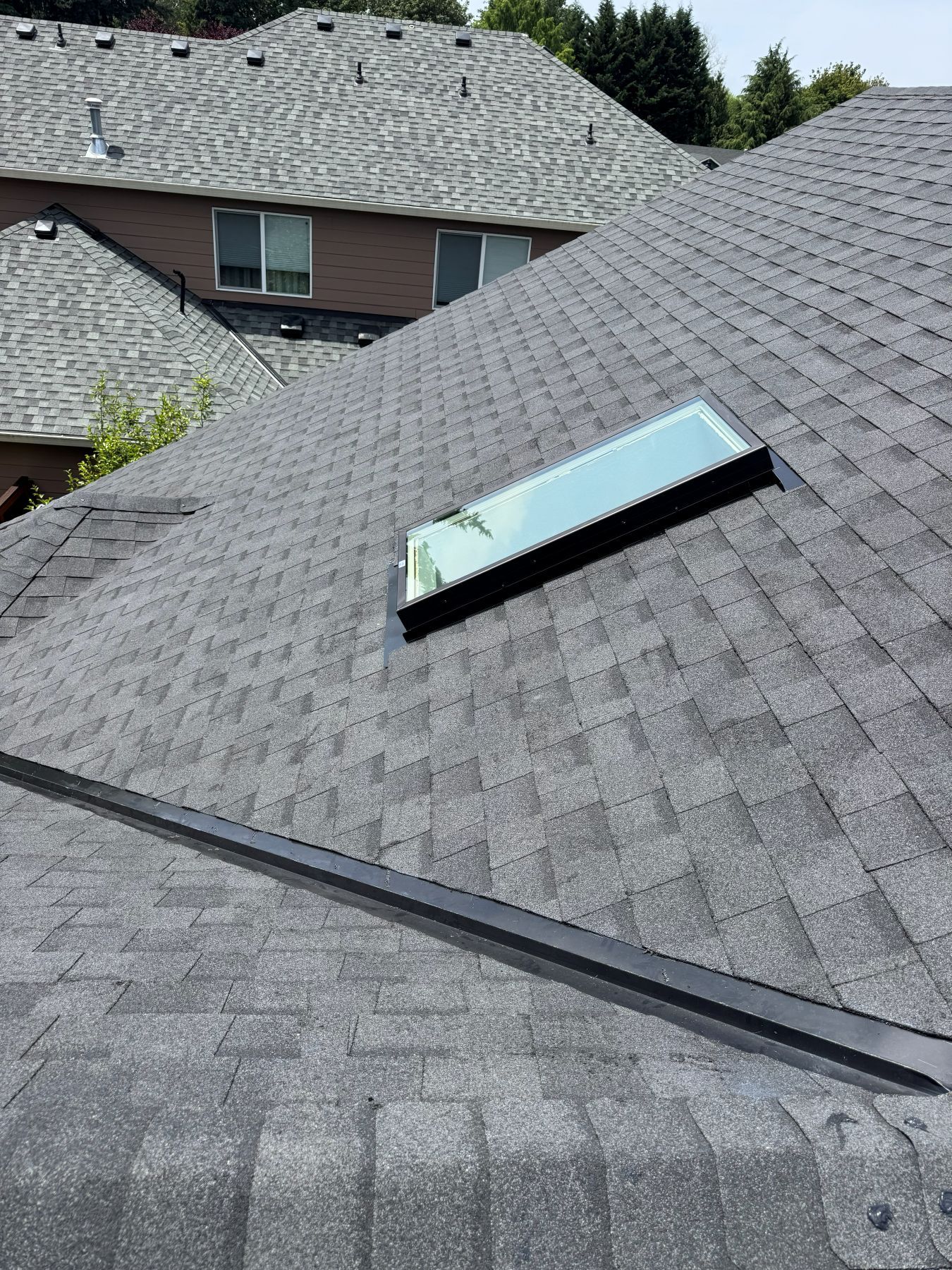 Roof with a damaged skylight and a bent gutter on a shingled house
