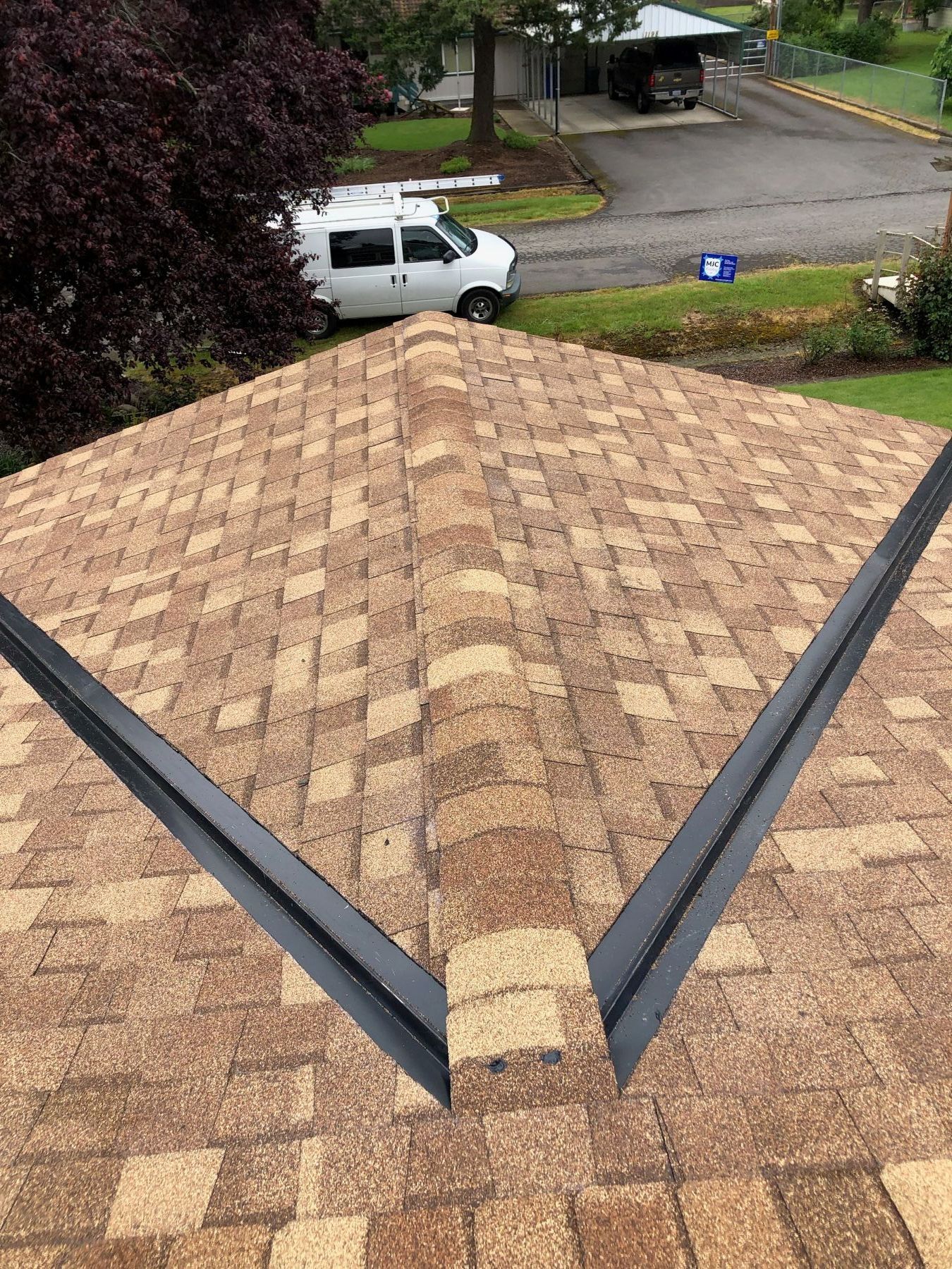 Roof shingles with a centered ridge vent, viewed from above, with a neighborhood street and white pickup below