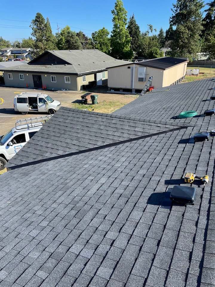 New gray shingle roof on a residential building, with trees and parked vehicles in the background