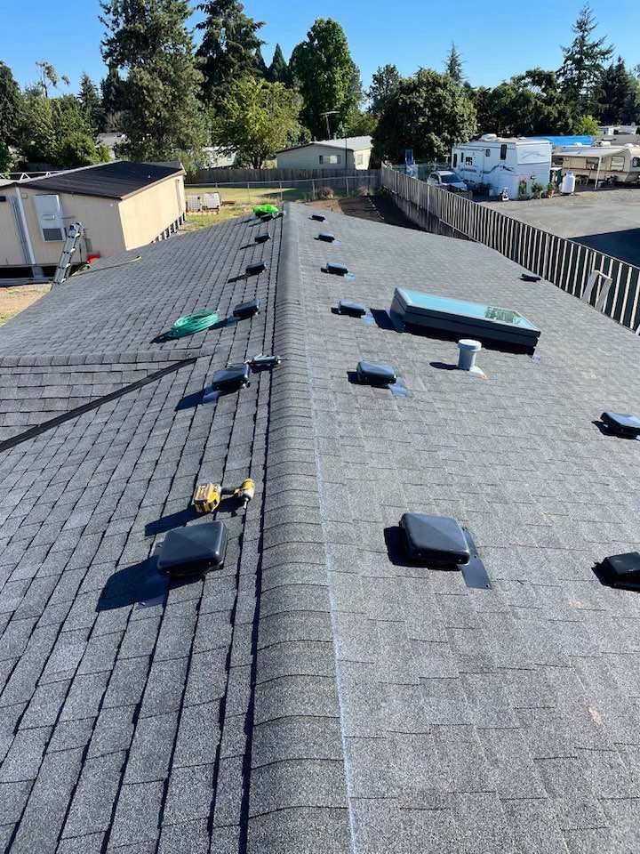 Rooftop with gray shingles, scattered tools and materials, viewed across a residential neighborhood.