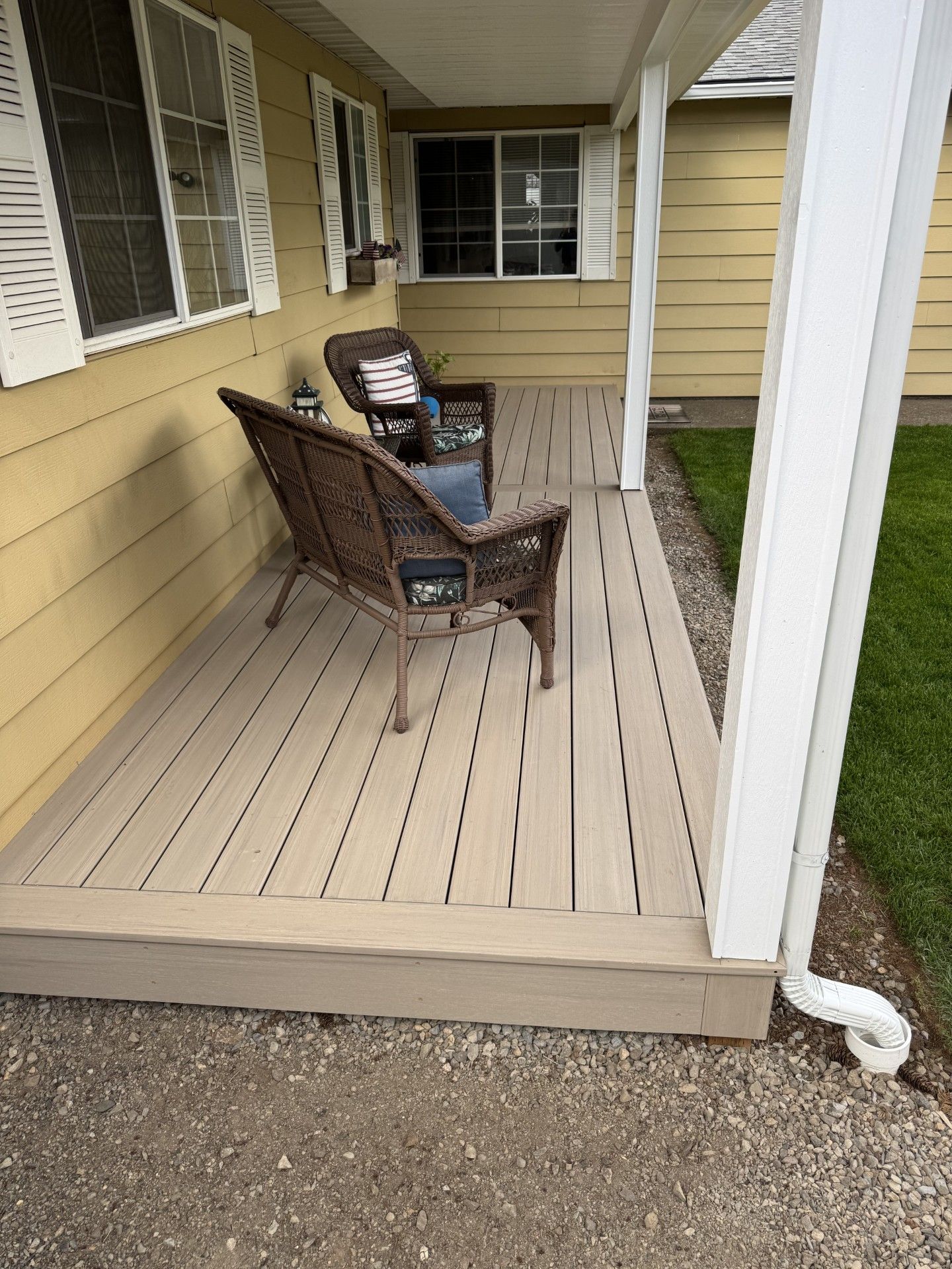 Covered porch with beige siding, two chairs, and a small table on a narrow wooden deck.