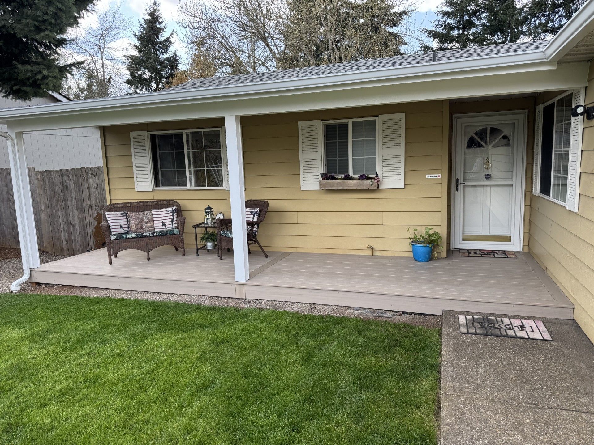 Front porch of a beige house with white columns, a bench, potted plant, and closed front door.