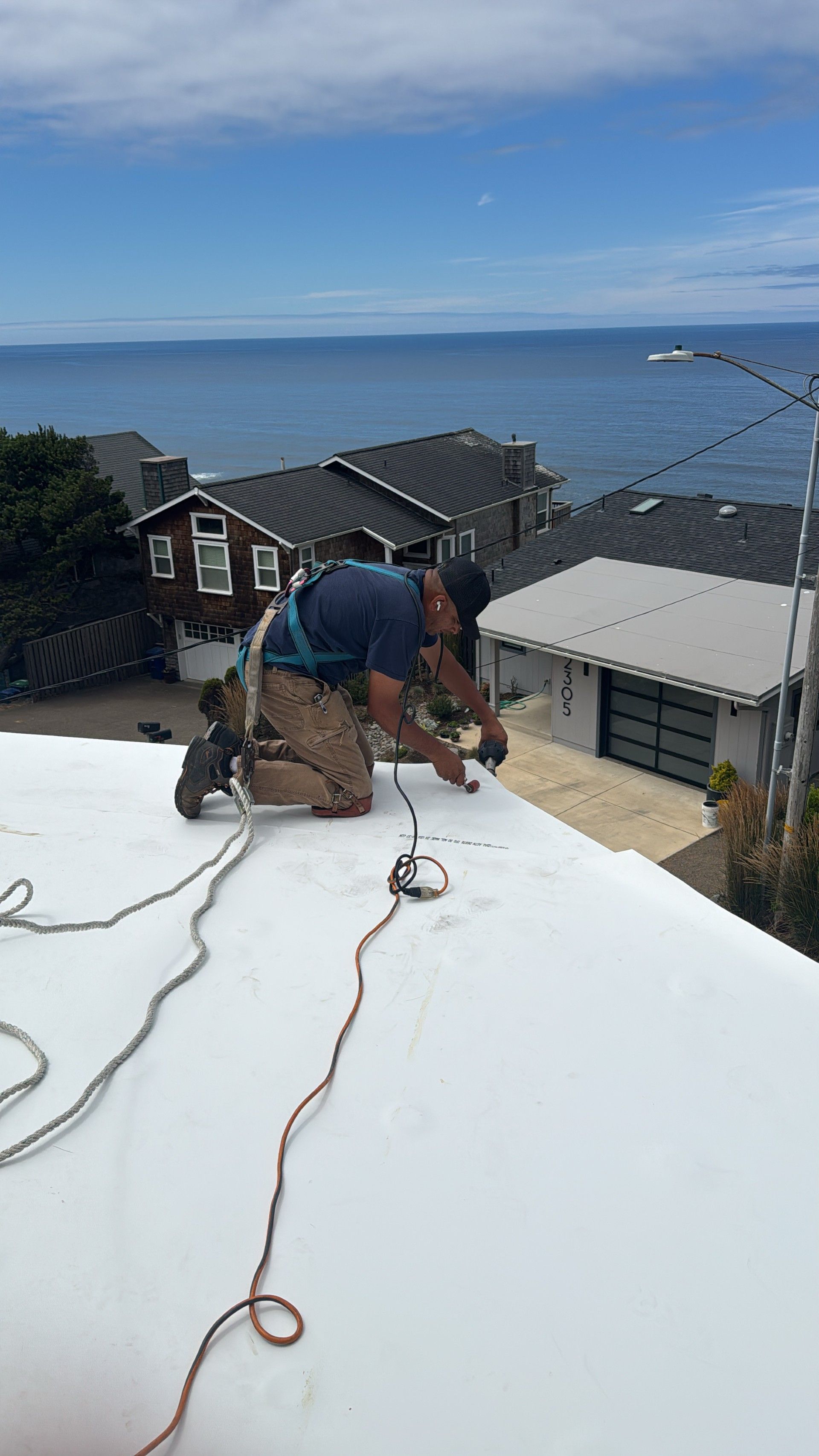 Worker repairing a white rooftop with ocean and houses in the background