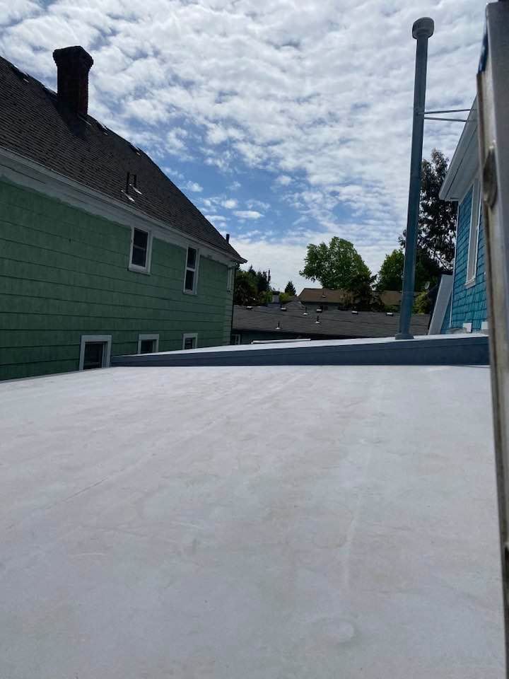 Flat white rooftop beside a green house and blue building under a cloudy sky