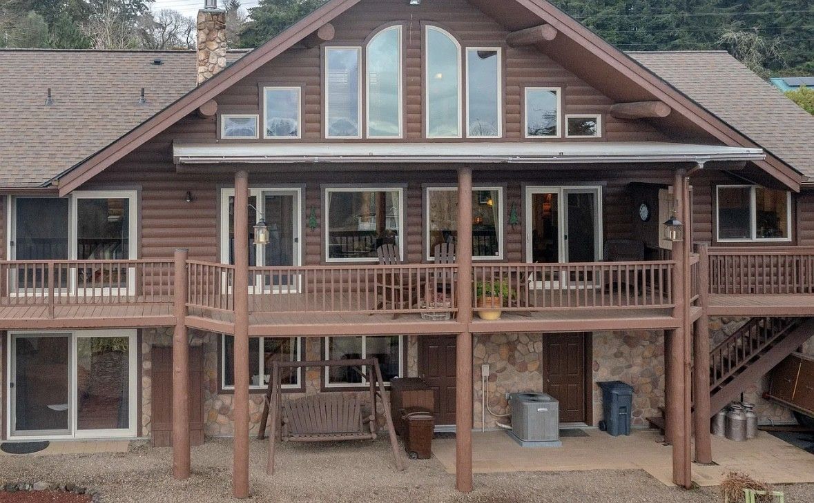 Wooden cabin with large front porch, elevated deck, and tall windows in a wooded setting