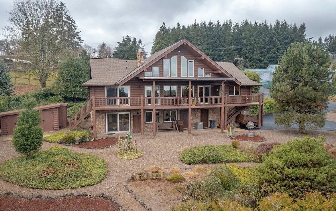 Large rustic log cabin with a front porch, surrounded by landscaped shrubs and trees
