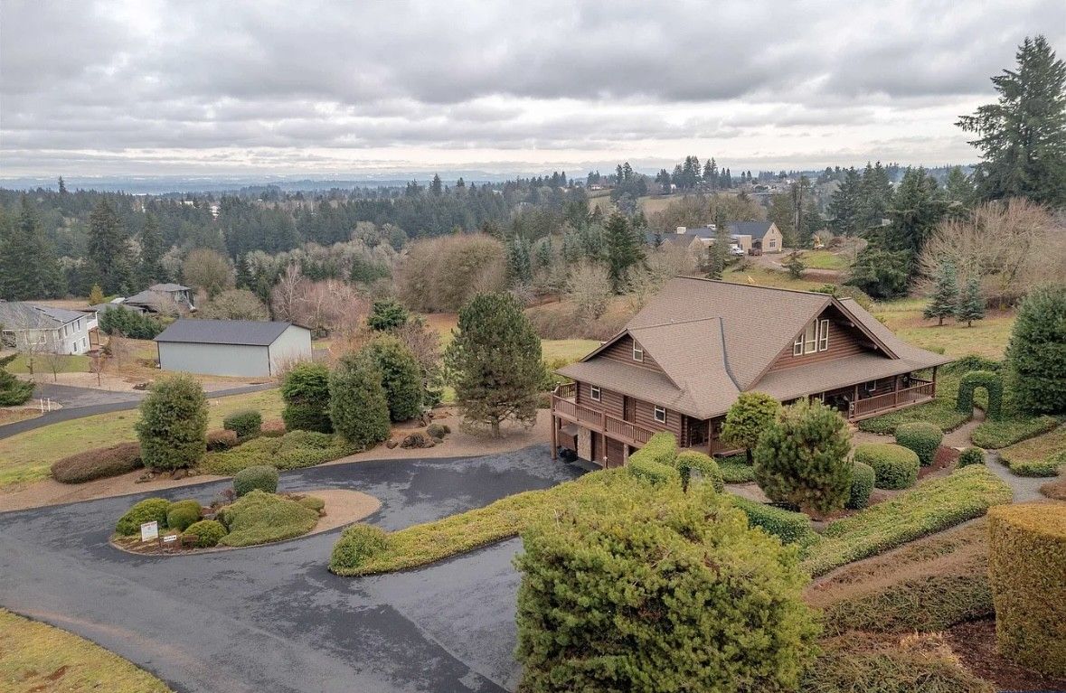 View of a landscaped hillside home with winding driveway under a cloudy sky