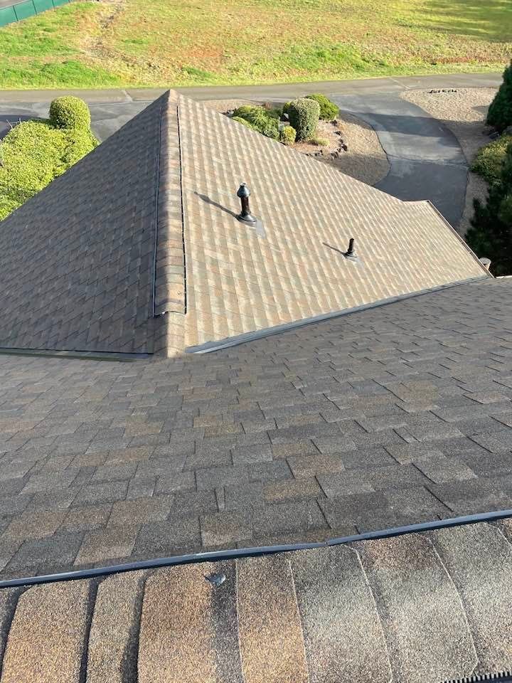 Roof with gray shingles and two vents, viewed from above next to a driveway and grassy yard