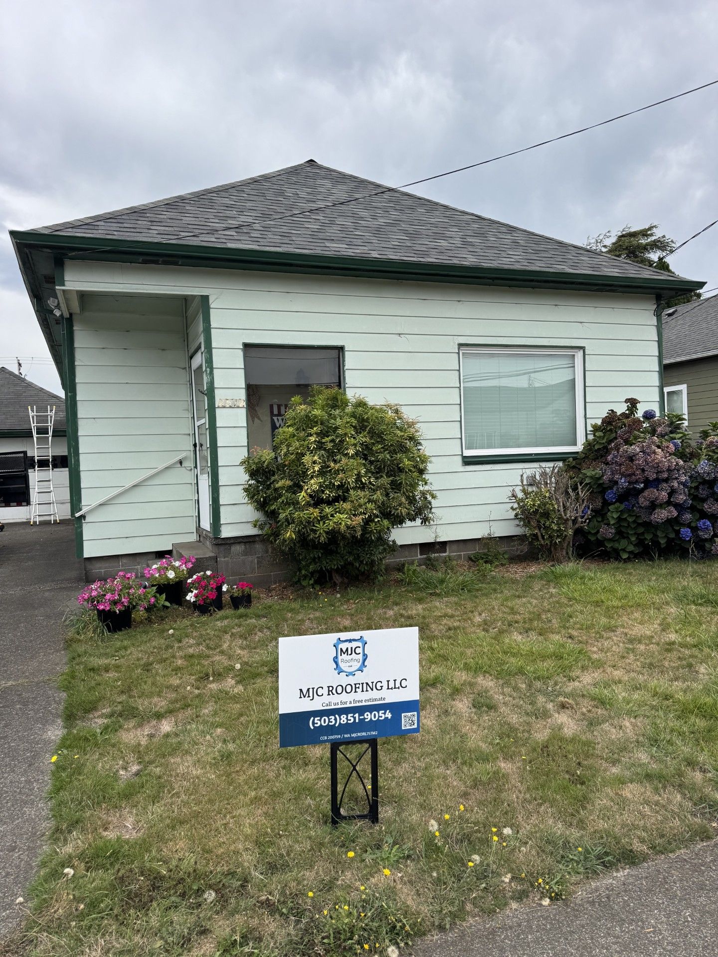 Small white house with gray roof and front yard; blue real estate sign in the grass.