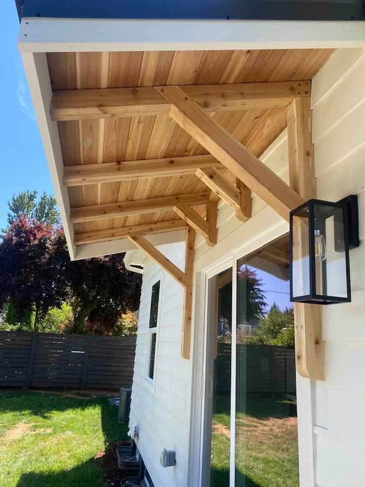 Wooden porch roof with exposed beams and white siding beside a backyard lawn and fence.