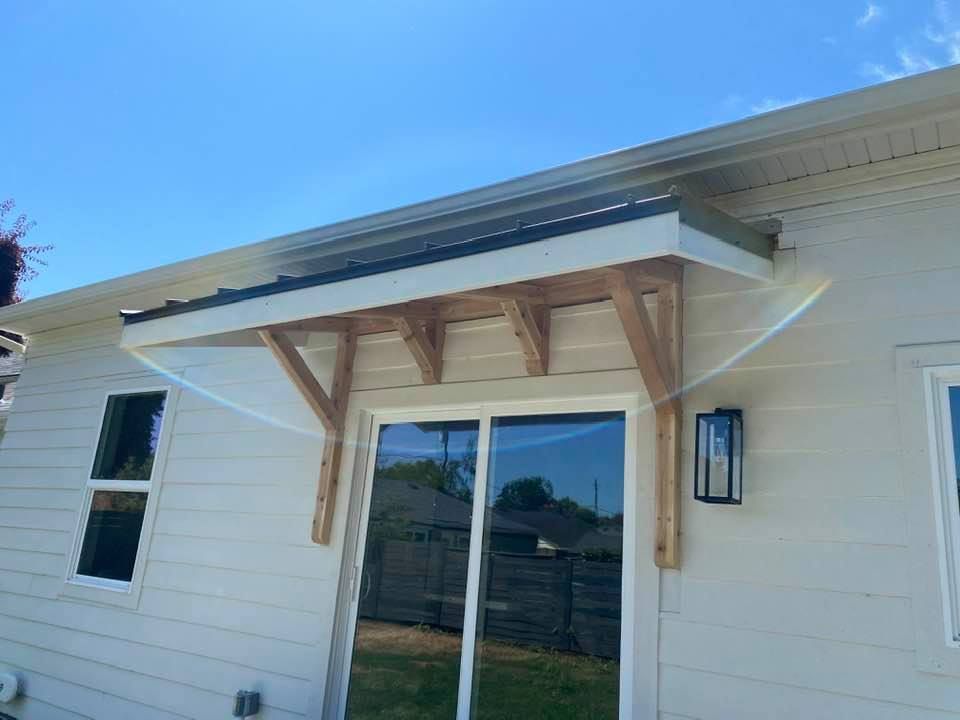 Small white house exterior with a wooden awning over a sliding glass door and lantern light fixture