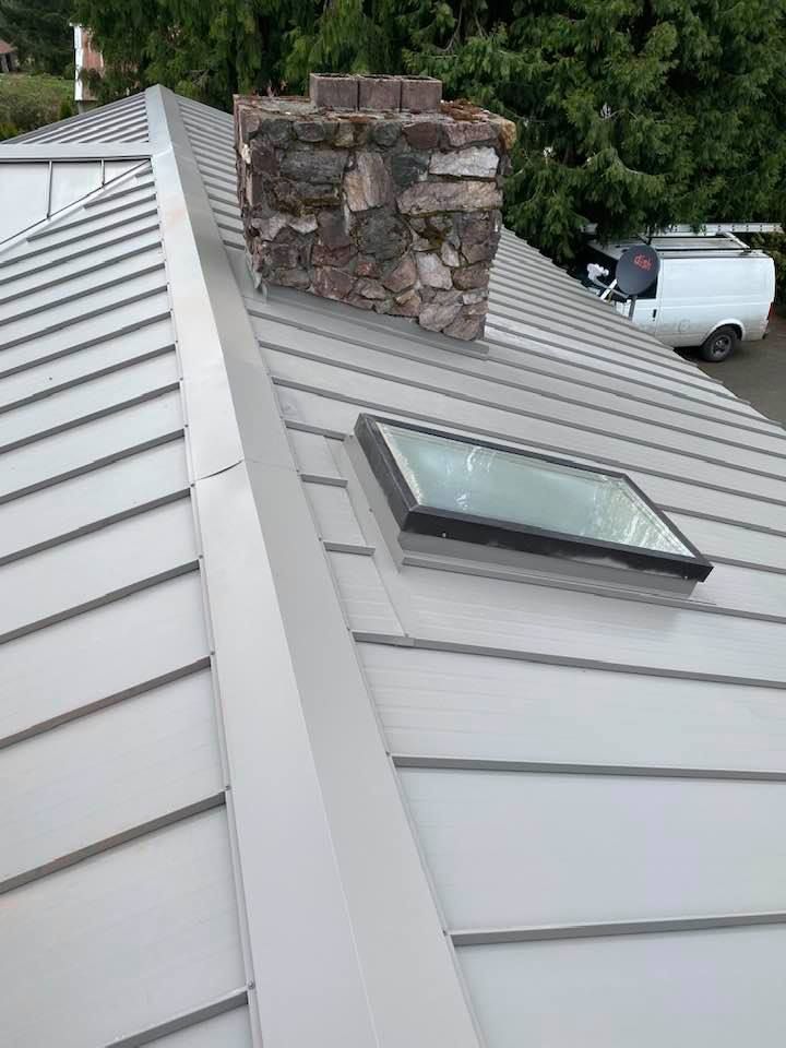 Rooftop skylight beside a stone chimney on a light gray metal roof