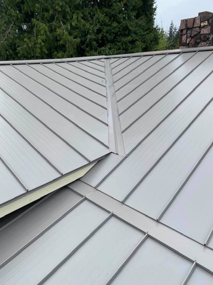 Close-up of a light gray metal roof with intersecting seams and a chimney at the top right