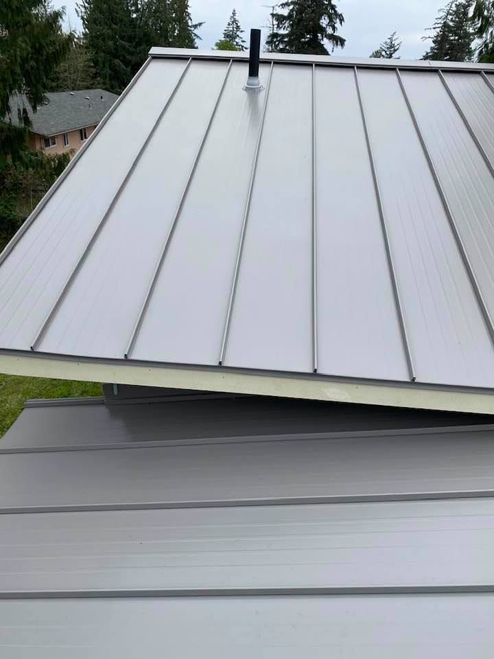 Metal roof with raised seams and a black vent pipe, viewed from above on a cloudy day