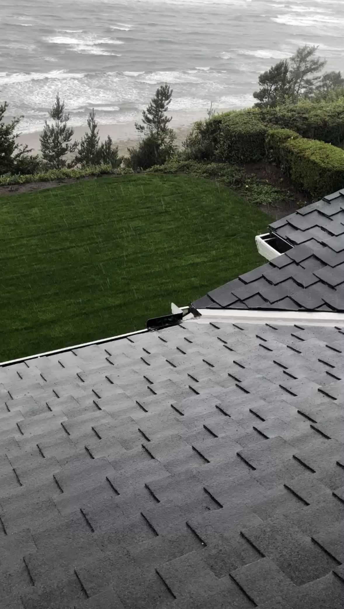 Gray shingled roof overlooking a green lawn, trees, and a misty waterfront beyond