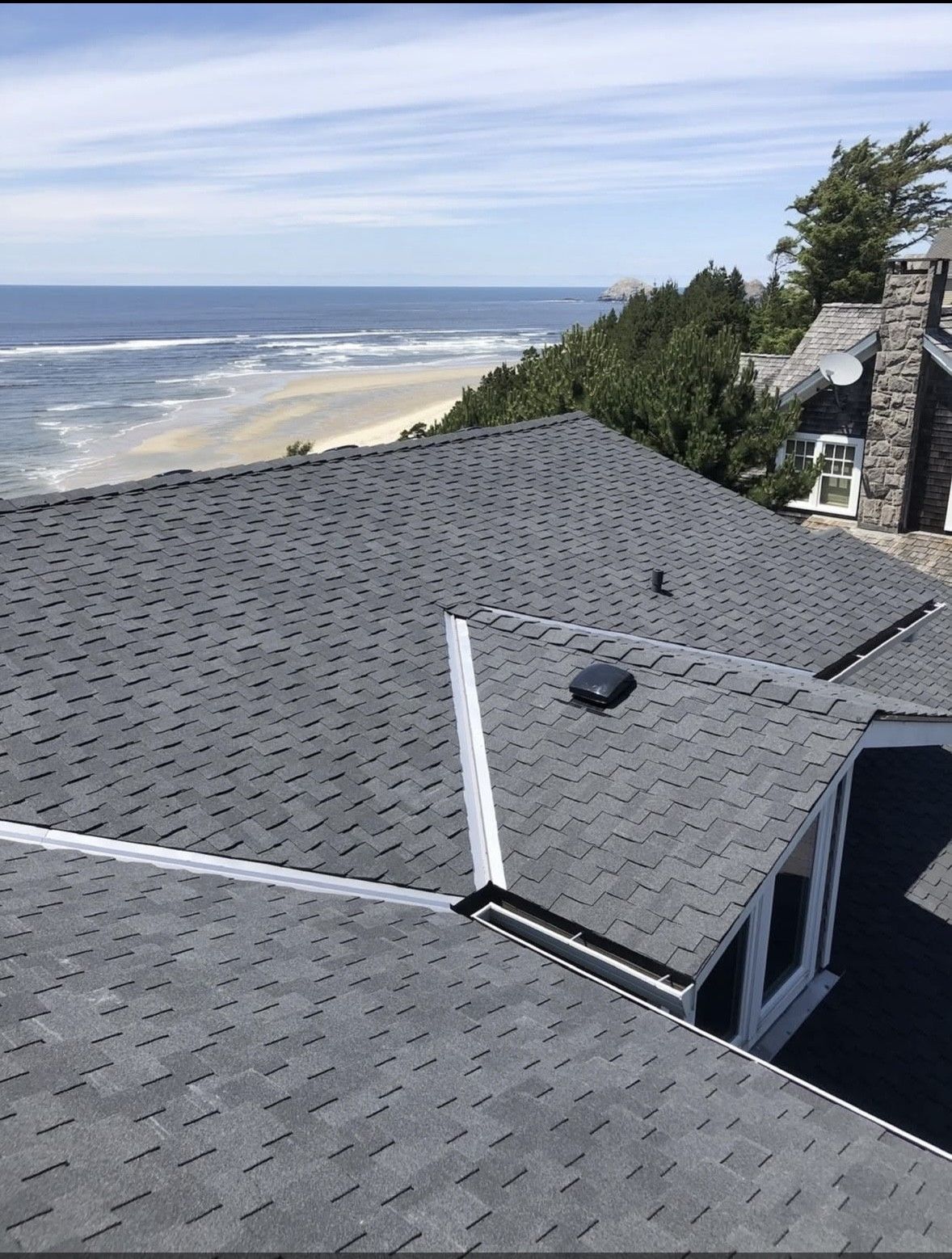 Coastal house roof with gray shingles beside the ocean on a sunny day