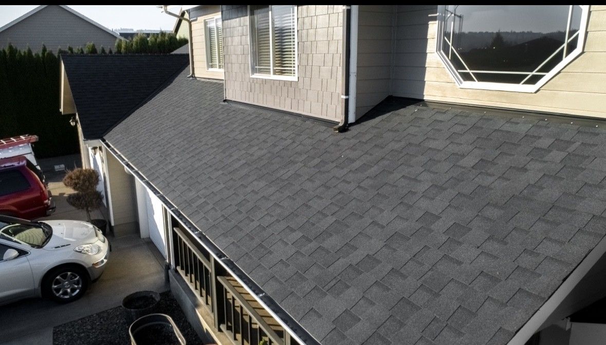 Roofing work on a gray house with dark shingles, viewed from above near parked cars