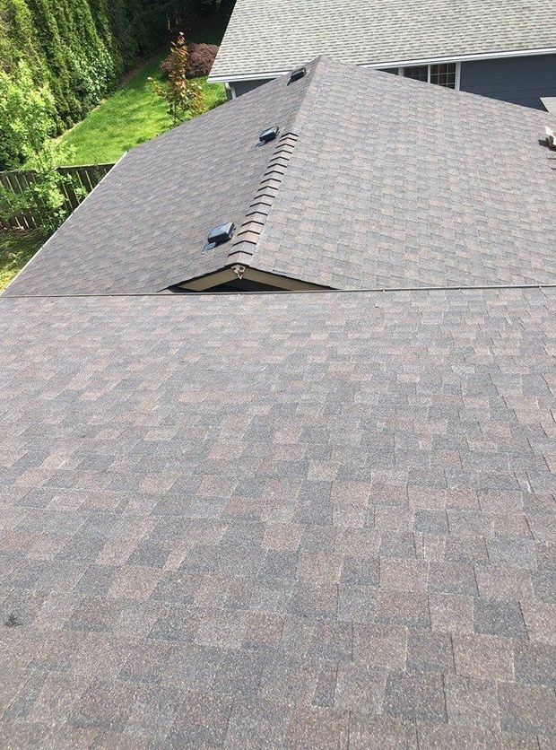 An elevated, high-angle view of brown asphalt shingle roofing with two vent caps and a small gable section.