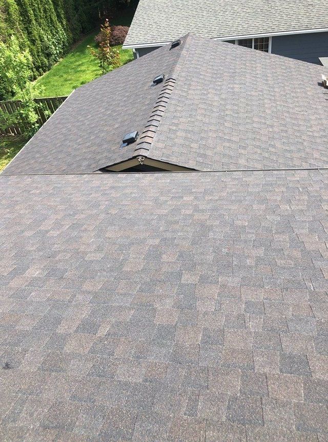 An elevated, high-angle view of brown asphalt shingle roofing with two vent caps and a small gable section.