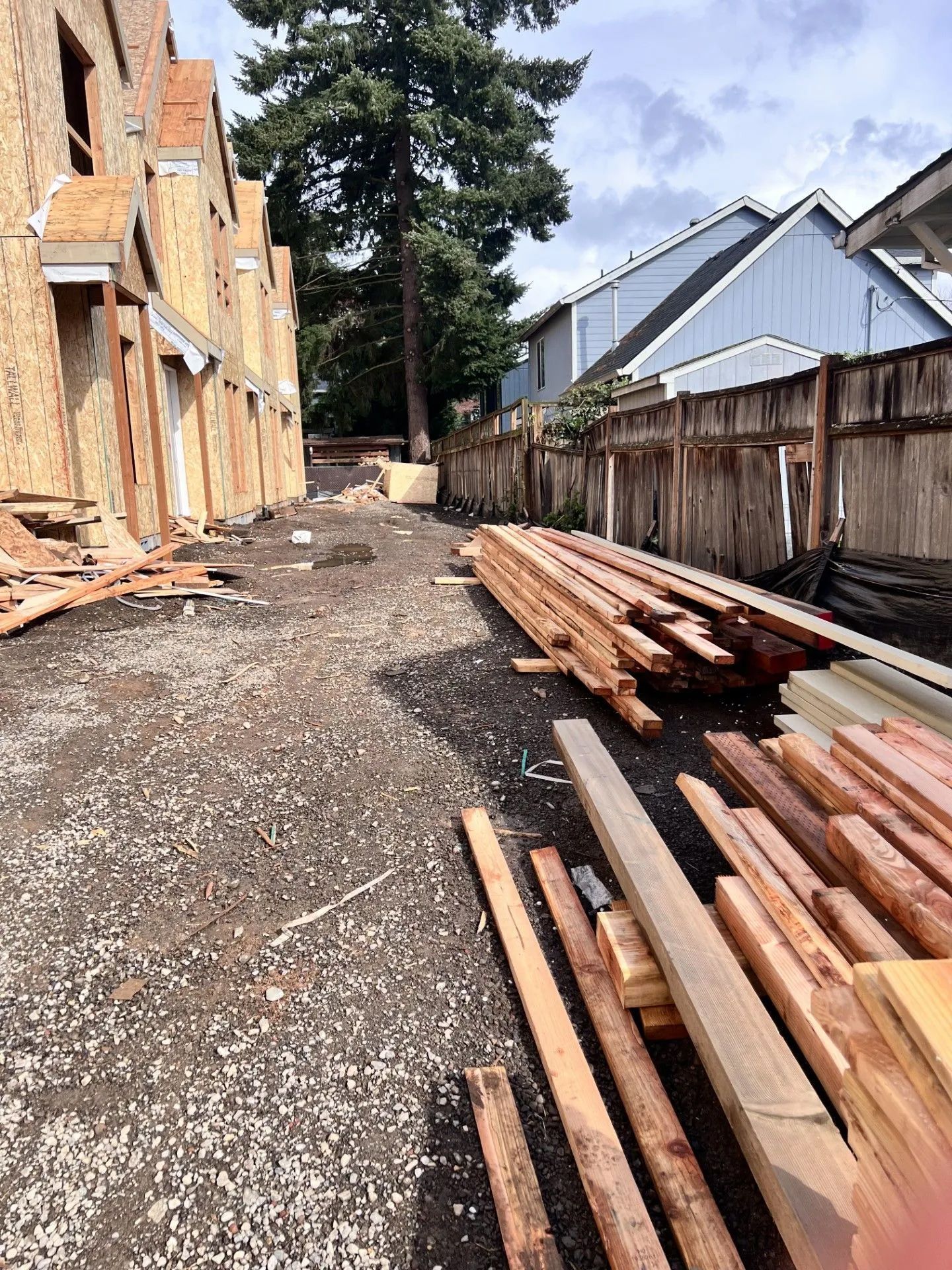 Construction site alley with stacked lumber, gravel ground, and houses on both sides