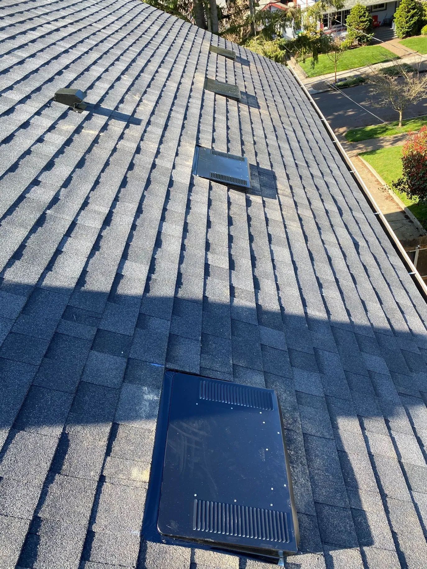 Shingled rooftop with three skylights on a sunny day, viewed from above