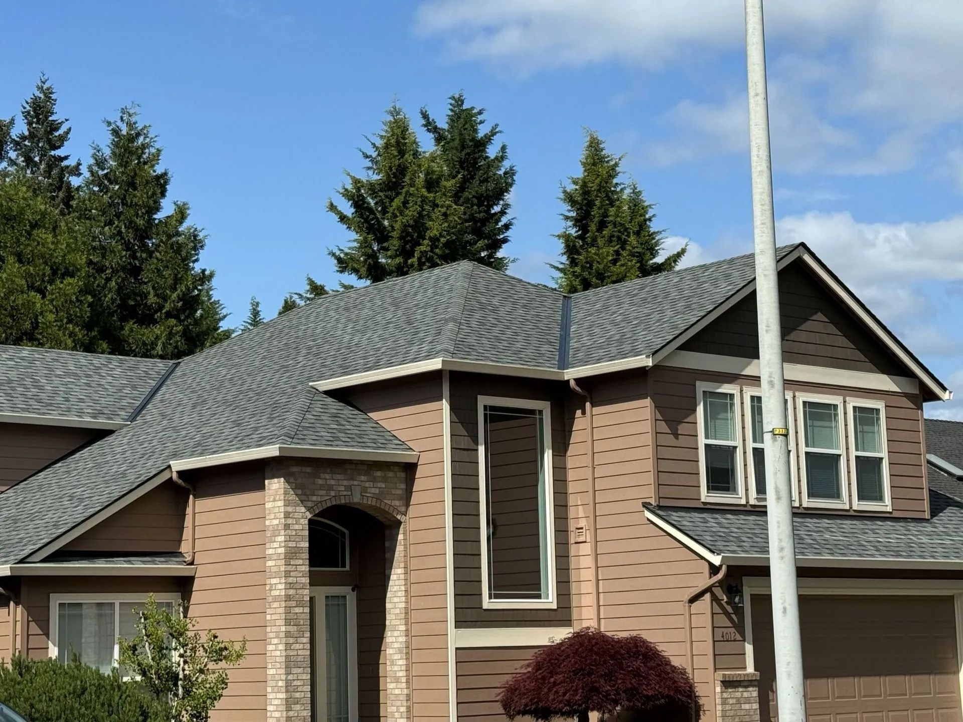 Suburban brick house with gray shingle roof, arched entry, and garage under a blue sky