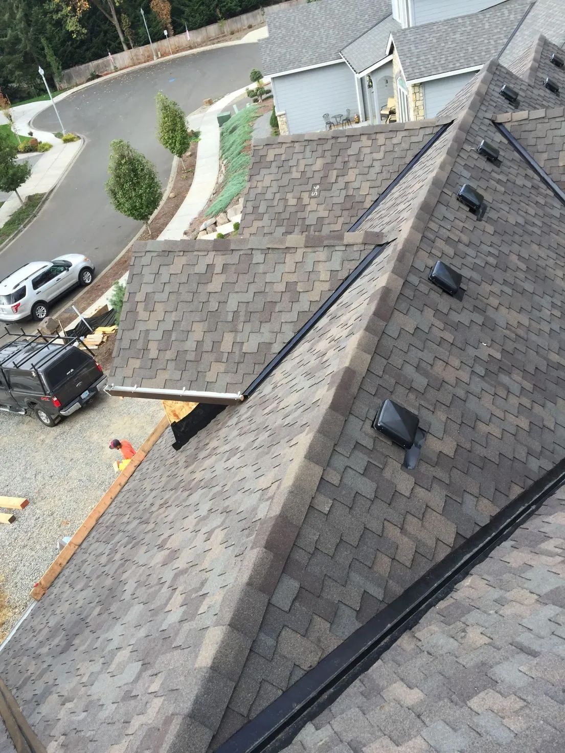 Roofing work on a shingled house roof, with workers and tools visible near the edge.