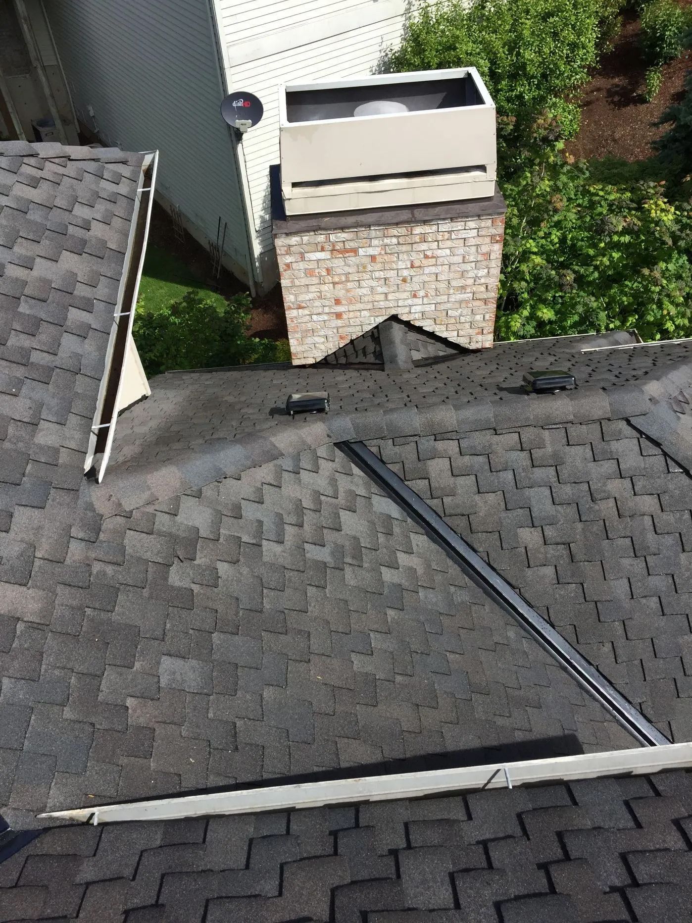 Roof view of a house with gray shingles, ridge vent, and a small brick chimney near the center.