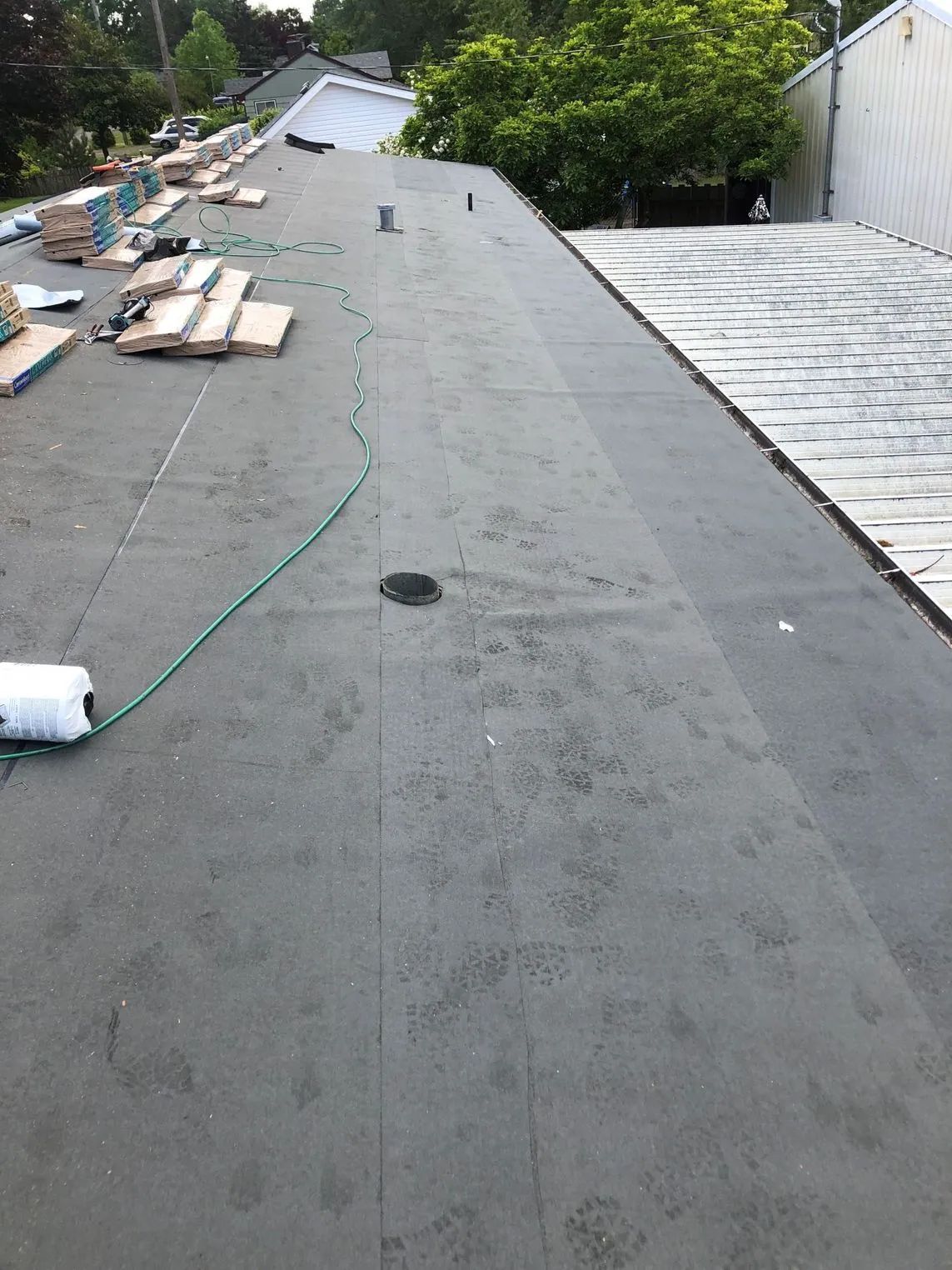 Flat gray roof under construction with lumber stacks and a green hose along the ridge