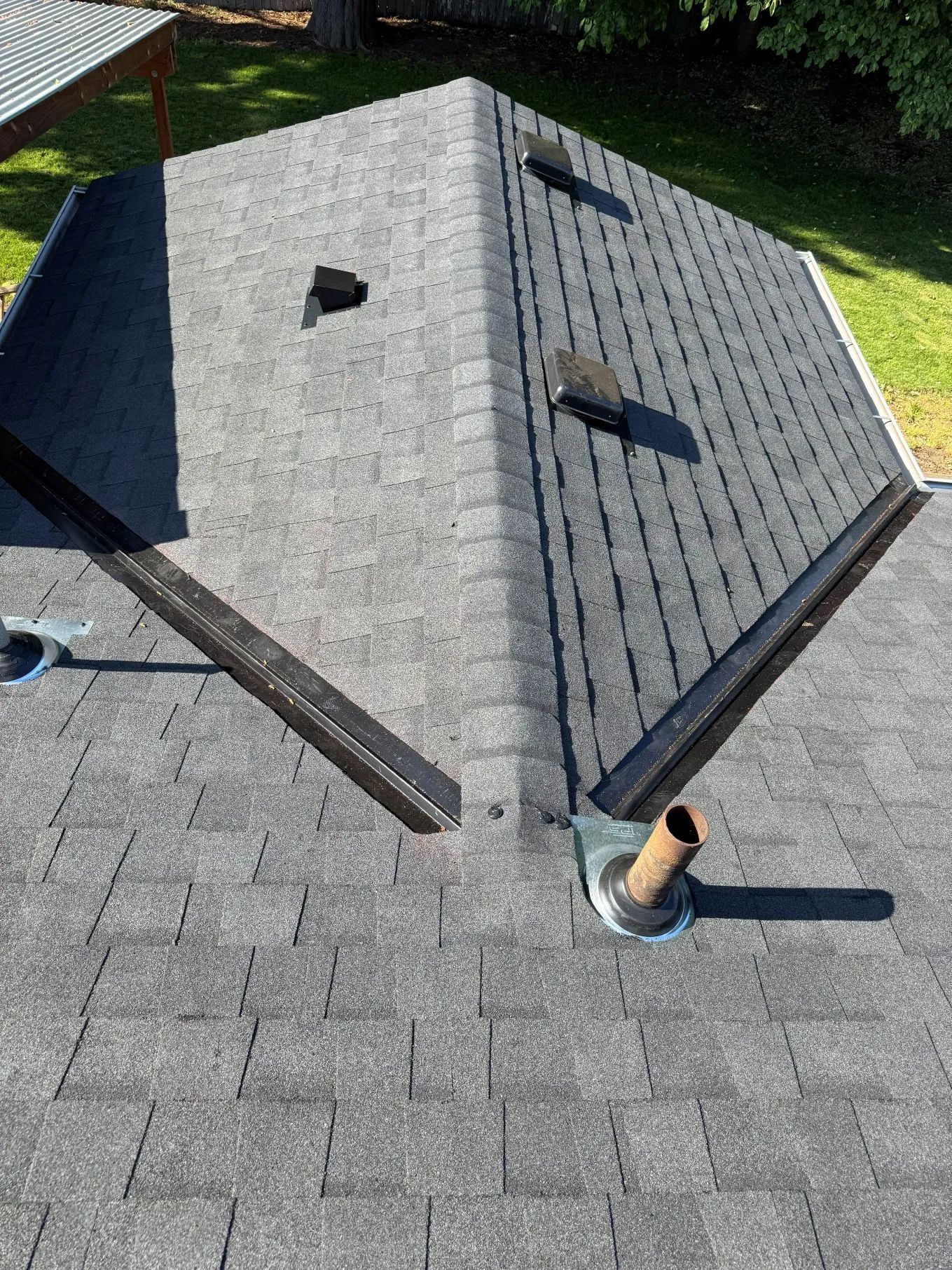 Rooftop with gray shingles, central vented structure, and two metal roof vents in sunlight