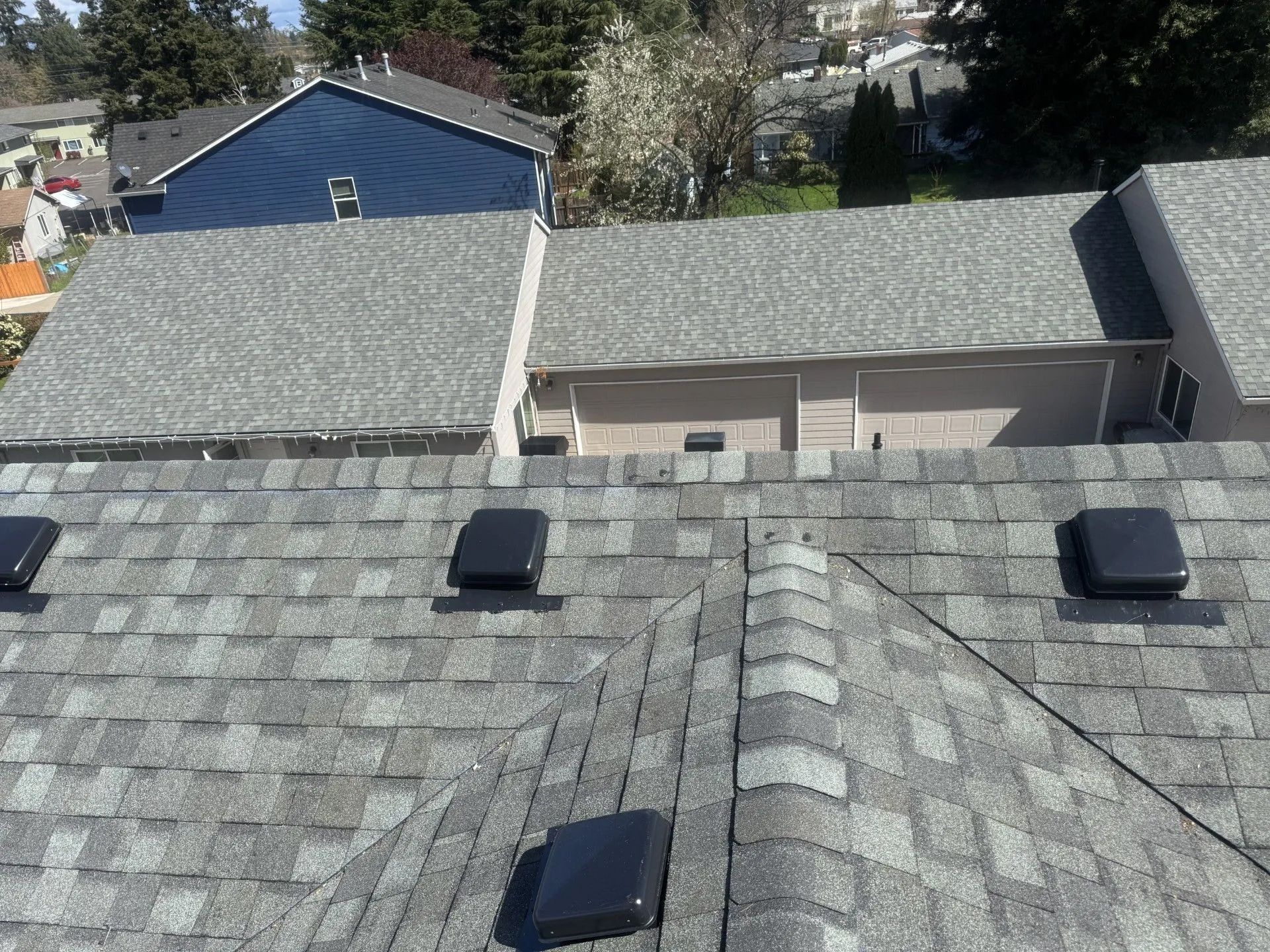 Rooftops with gray shingles and three black vents under bright daylight, viewed from above.