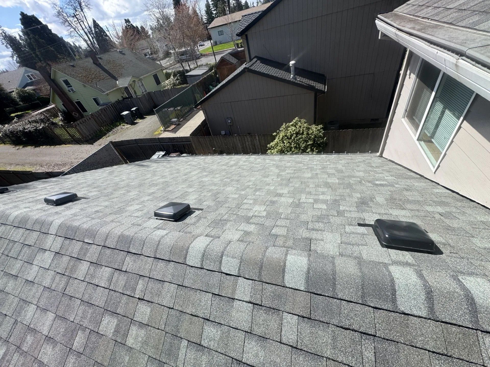 Rooftop with gray shingles and three vents, overlooking neighboring houses on a sunny day