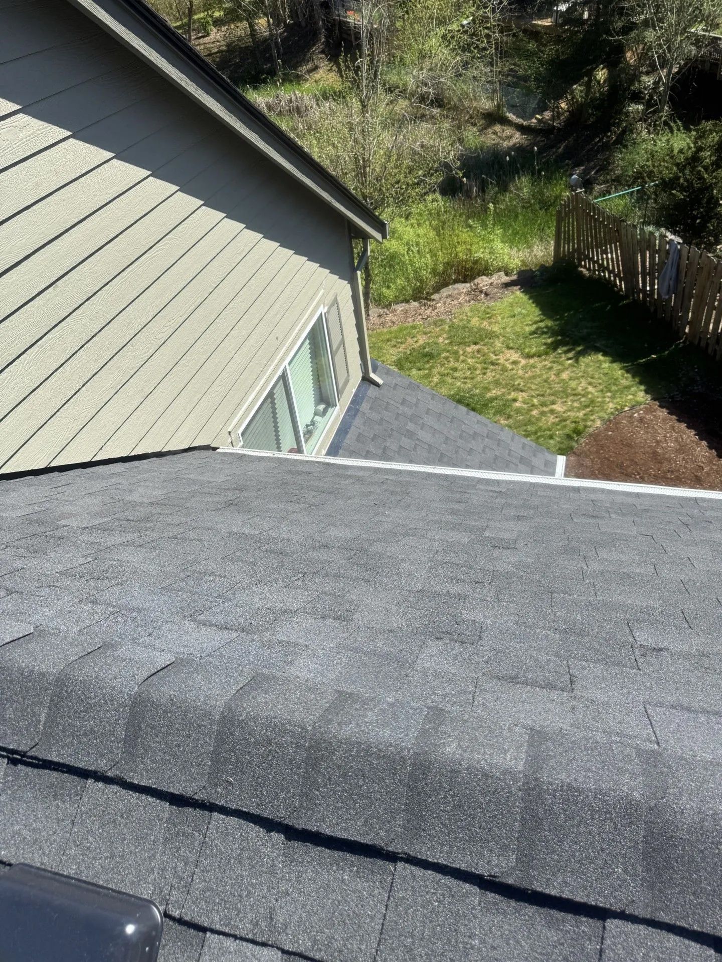 Roof view of a house with gray shingles, beige siding, and a backyard fence below.