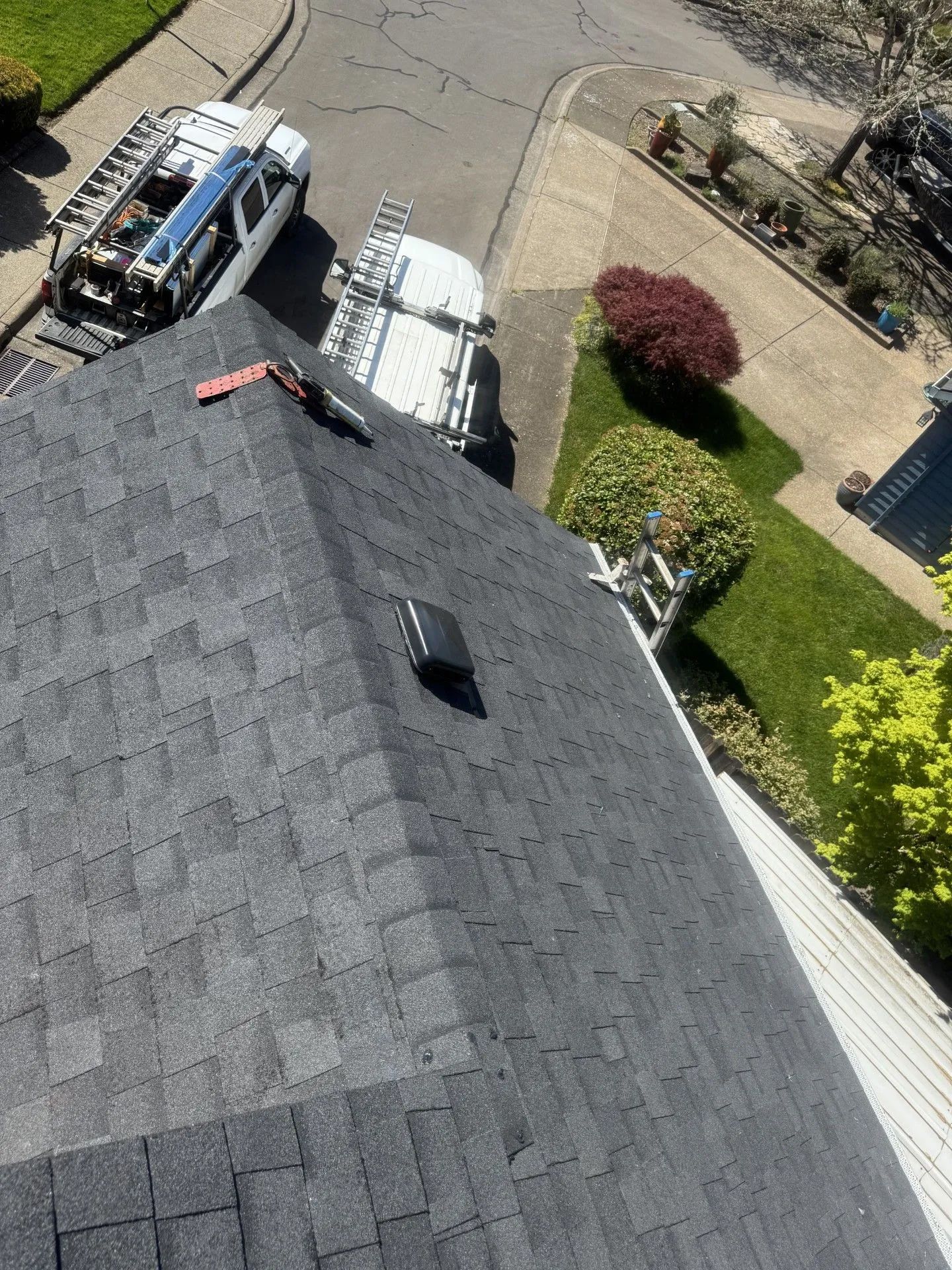 Roof view with two work vans parked by a house and a landscaped driveway below.