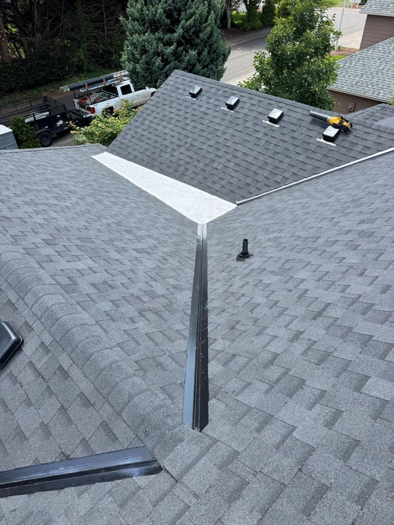 Roof valley with gray shingles and roof vents, viewed from above