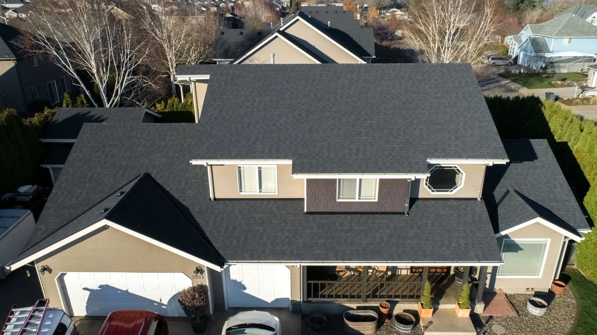 Aerial view of a suburban house with dark roof, beige siding, and a two-car garage.