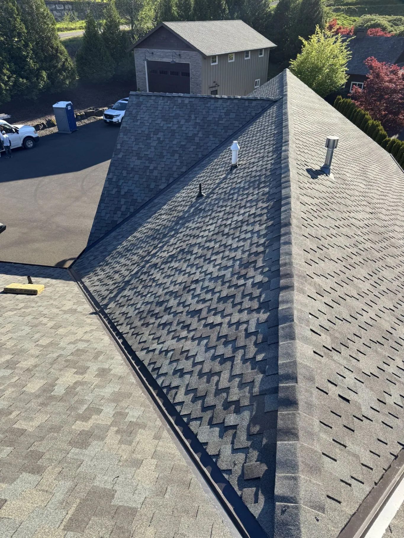 Aerial view of a shingled roof with a long ridge vent and a small rooftop vent in a suburban neighborhood.