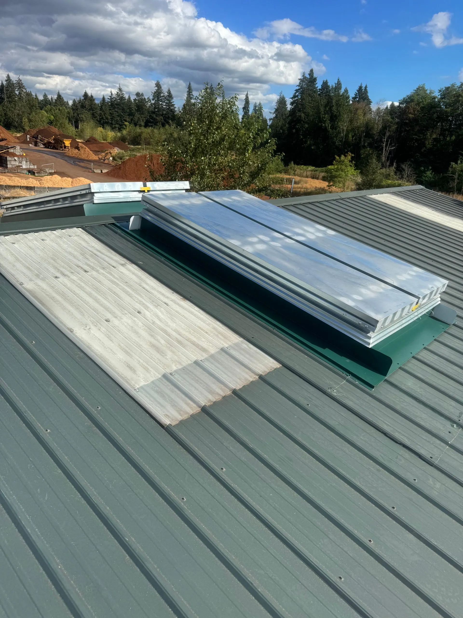 Rooftop skylight vents on a green metal roof with trees and sky in the background