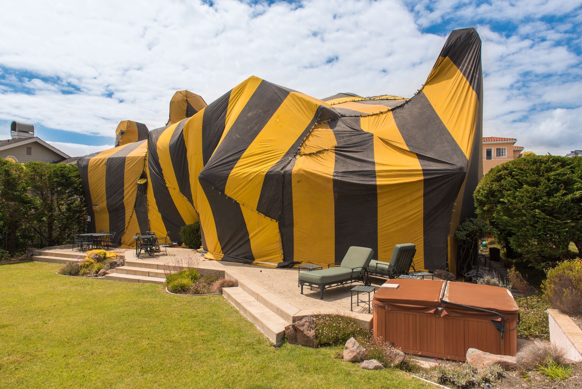 Yellow-and-black striped inflatable building on a lawn with patio furniture and hedges