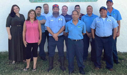 Group of people posing outdoors in front of a white wall, wearing blue shirts and dark uniforms.