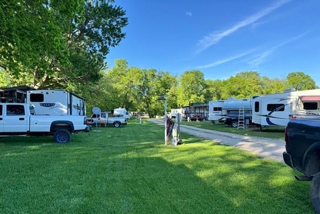 RV park with lush green grass, big shade trees and a pretty blue sky with white streaky clouds