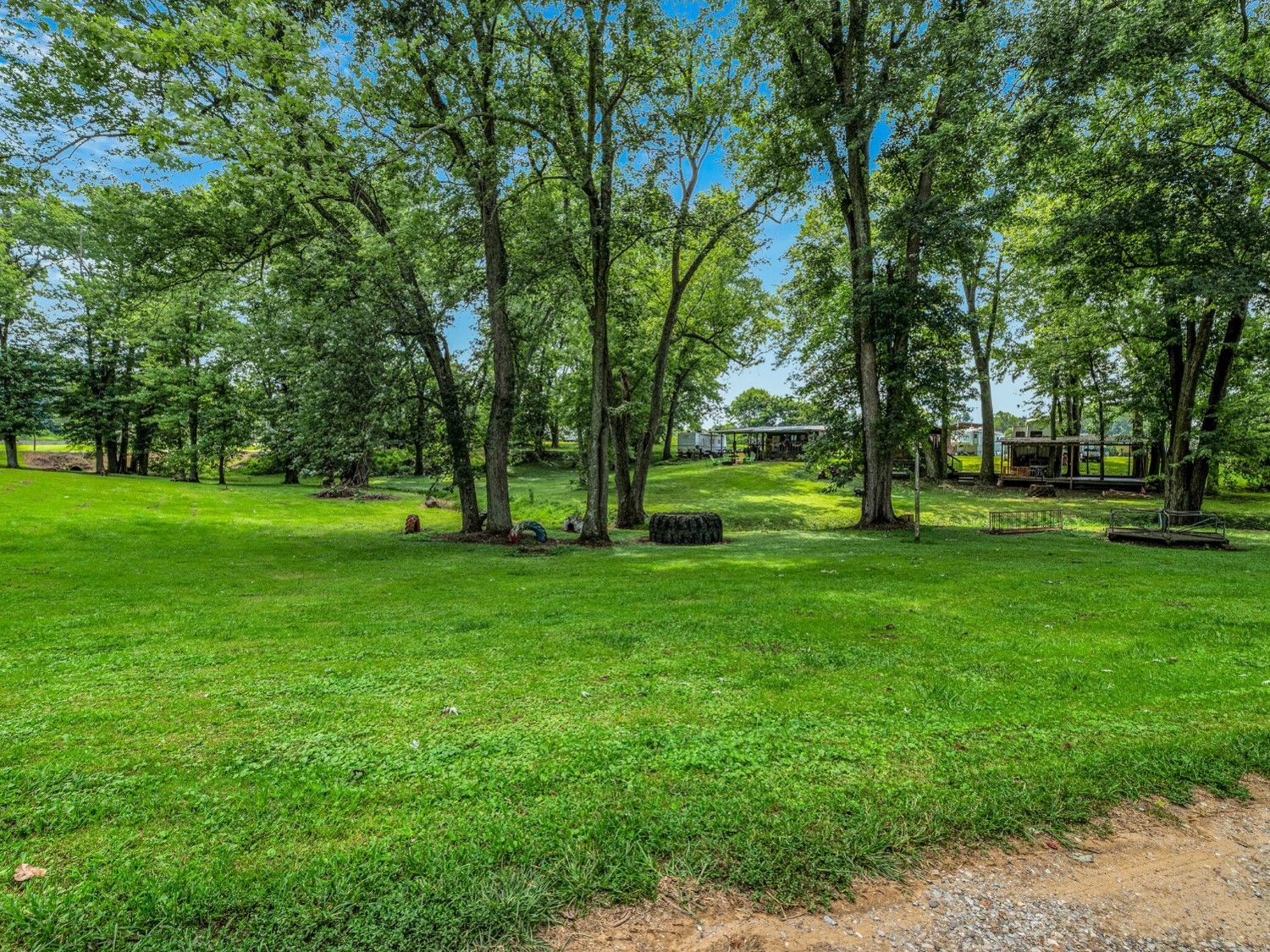 A large lush green field surrounded by trees and a dirt road.