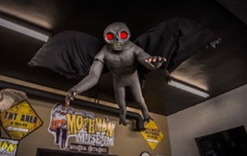 A statue of a bat with red eyes is hanging from the ceiling of a museum.