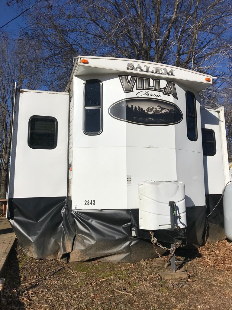 A white rv is parked in a field with trees in the background.