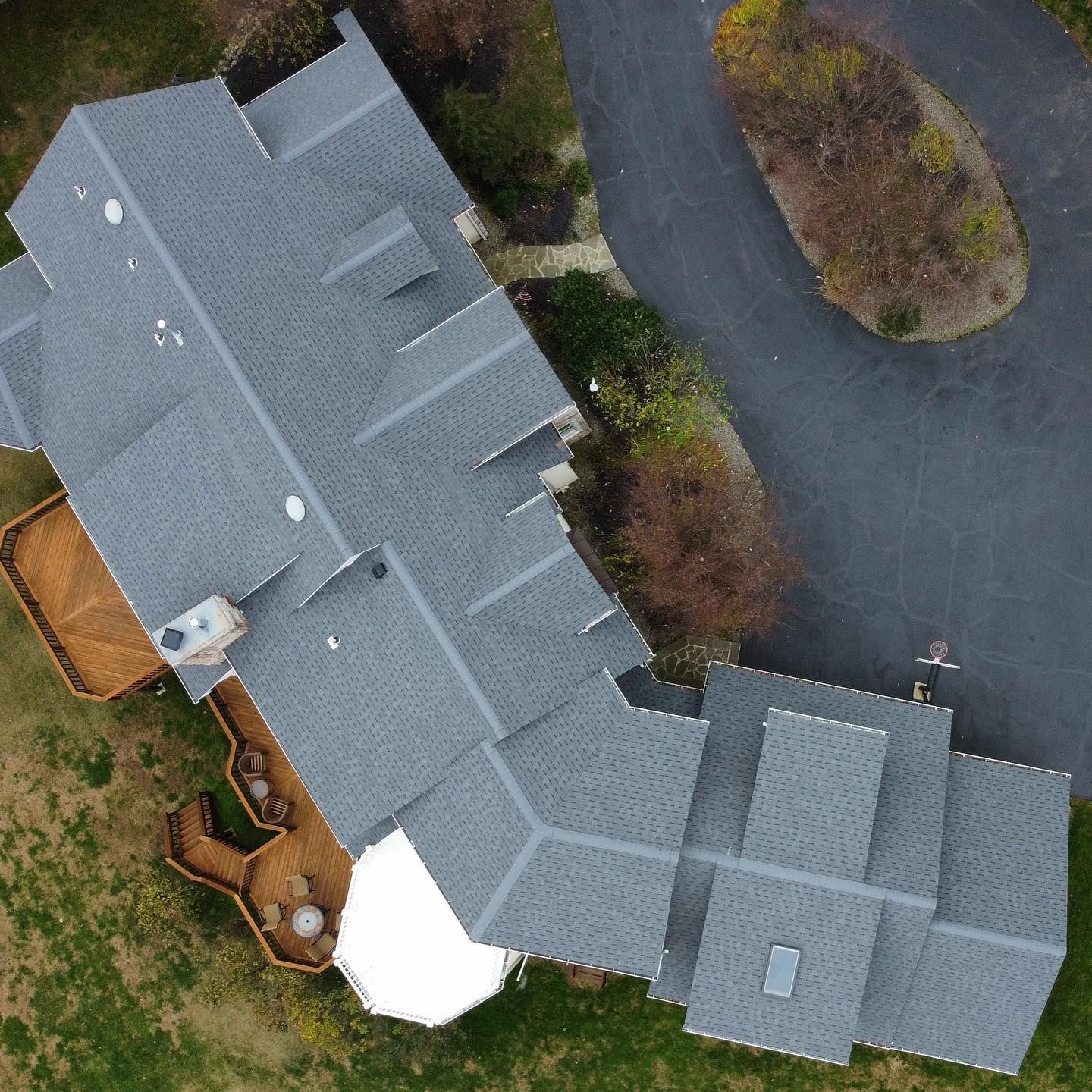 Aerial view of a gray-roofed house with a curved driveway and a small, wooded area.
