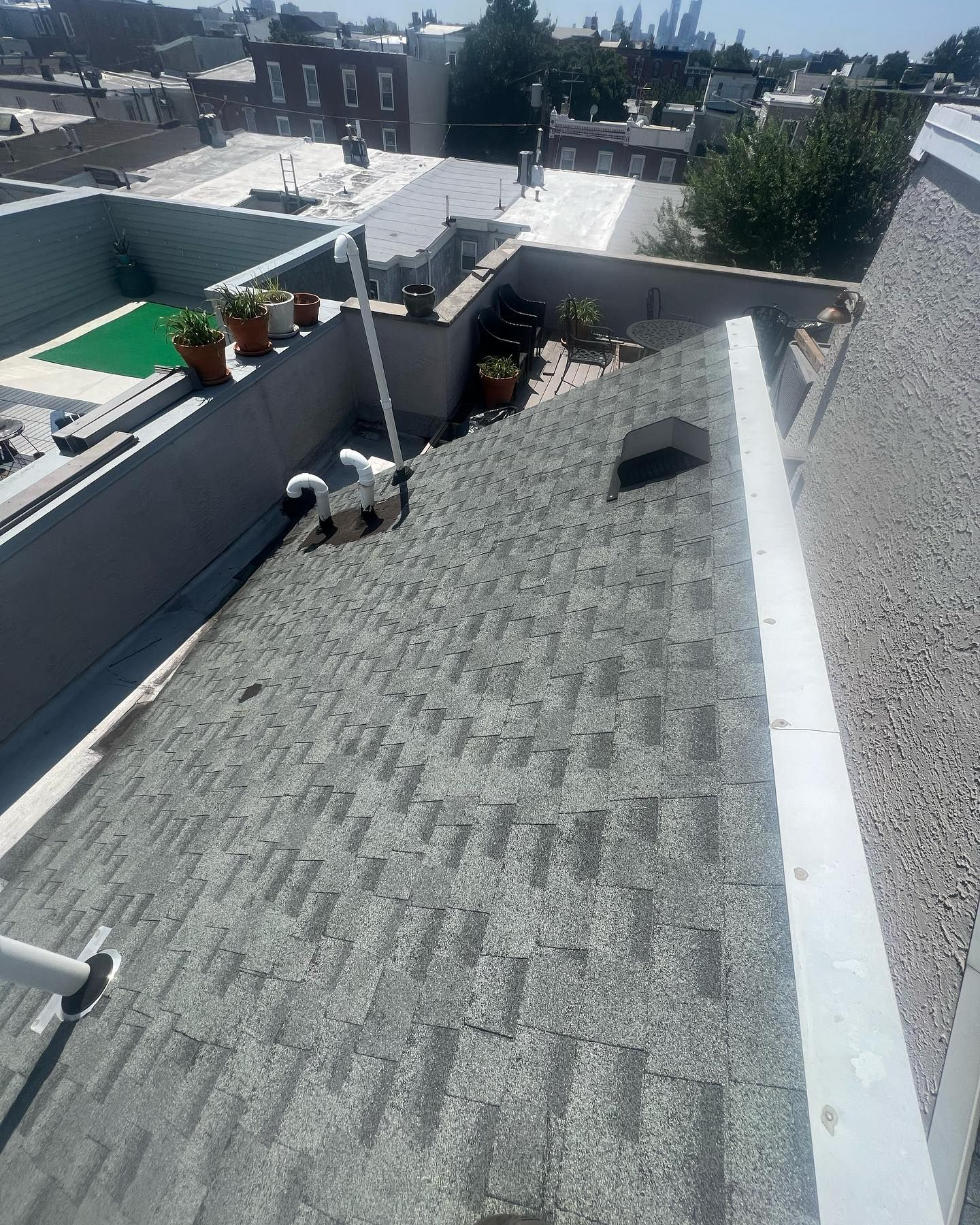 Rooftop with gray shingles, white trim, and a small garden area; city buildings in background.